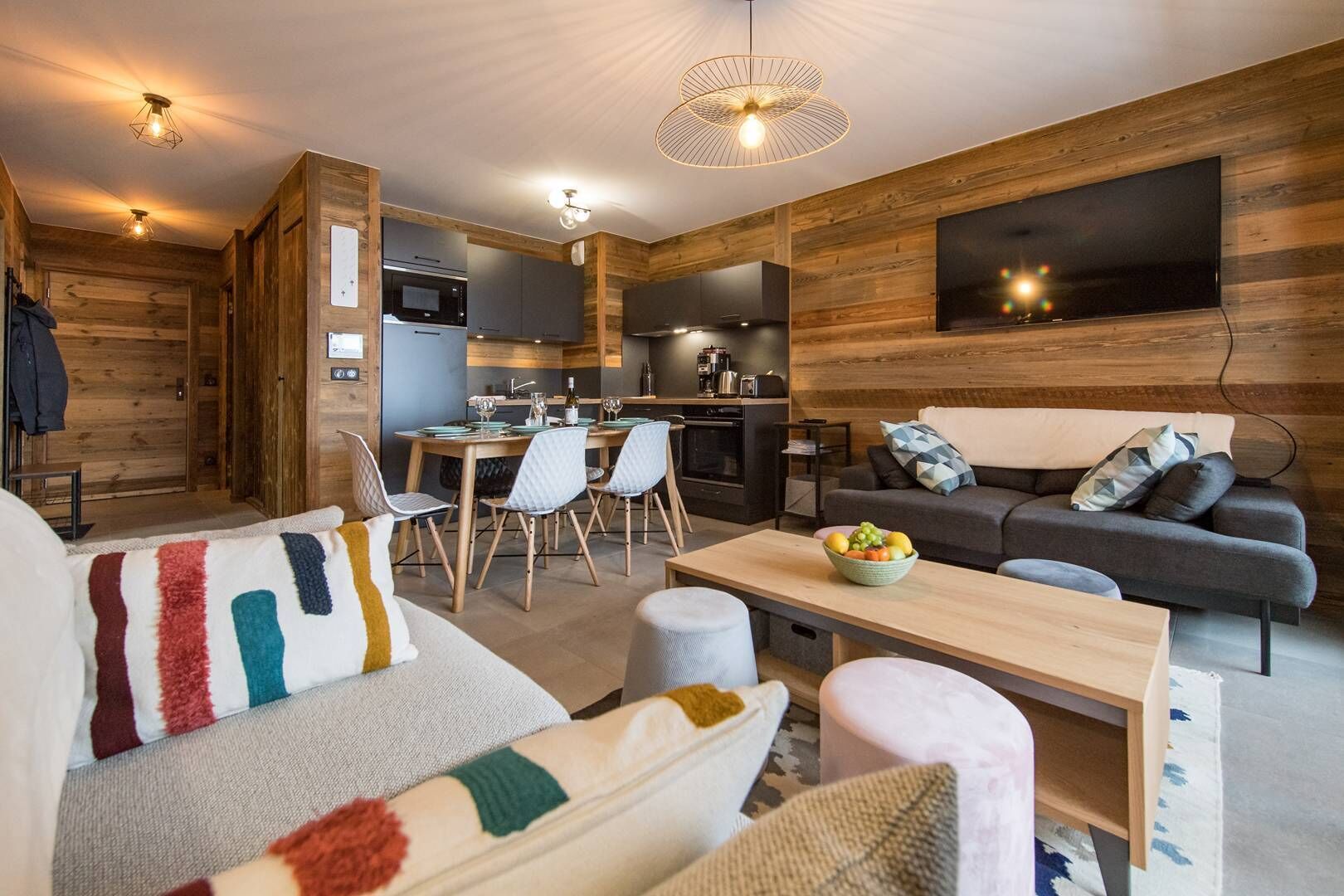 Uma sala de estar moderna com sofá, mesa de jantar e área de cozinha com paredes de madeira e uma televisão de tela plana.