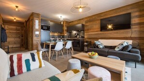 Een moderne woonkamer met een bank, een eettafel en een keukenhoek, met houten wanden en een flatscreen televisie.