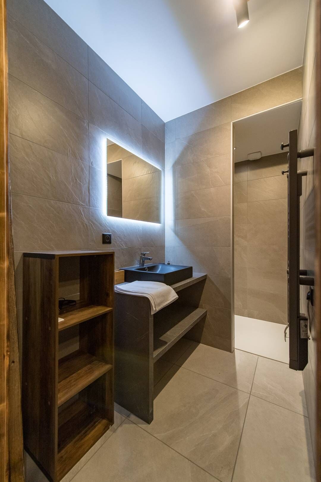 Une salle de bain moderne avec un meuble-lavabo en bois, un grand miroir et une douche à l’italienne.