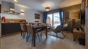 A modern kitchen with a dining area, stone wall, and large windows. - Olvera 203 - New apartment at the foot of the slopes (VALMEINIER)