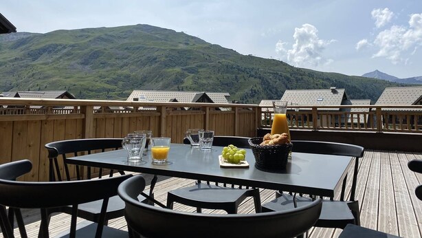 A wooden deck with a table set for breakfast, including a glass of orange juice, a pitcher, and a basket of grapes. - Olvera 203 - New apartment at the foot of the slopes (VALMEINIER)