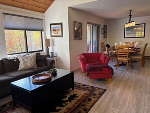 Un salon avec un canapé, une table basse et un fauteuil rouge. On y trouve également un coin repas avec une table dressée pour quatre personnes.