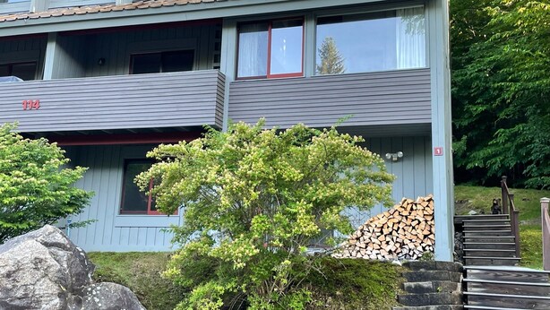 Een meerlaags gebouw met een grijze gevel, nummer 114, met balkons, grote ramen en een kleine buiten trap naar een houten terras.