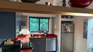 Een kleine keuken met een raam, roestvrijstalen apparatuur en een rode aanrechtblad.