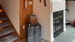 Een trap met houten treden die uitkomt op een plateau, met een open haard en een ski-rek aan de muur.