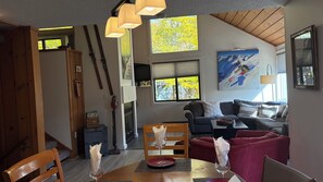 Un salon chaleureux avec un plafond en bois, un canapé, une table avec un verre à vin et un tableau représentant un skieur.
