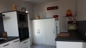 Moderni keittiö, jossa on valkoiset kaapit, sisäänrakennettu uuni ja mikroaaltouuni. Työtasoilla on koriste-esineitä ja hyllyllä punainen kattila.