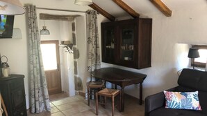 A cozy living room with a dark wooden table, a black sofa with a colorful pillow, and a rustic stove. - Typical Cévenol Mazet with magnificent view (Saint jean du gard)