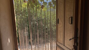 A wooden door with a metal handle and a keyhole, leading to an outdoor area with a metal grate and a view of greenery. - Typical Cévenol Mazet with magnificent view (Saint jean du gard)