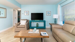 Een woonkamer met een blauwgroene salontafel, een beige bank, een houten salontafel en een televisie op een blauwgroene dressoir.