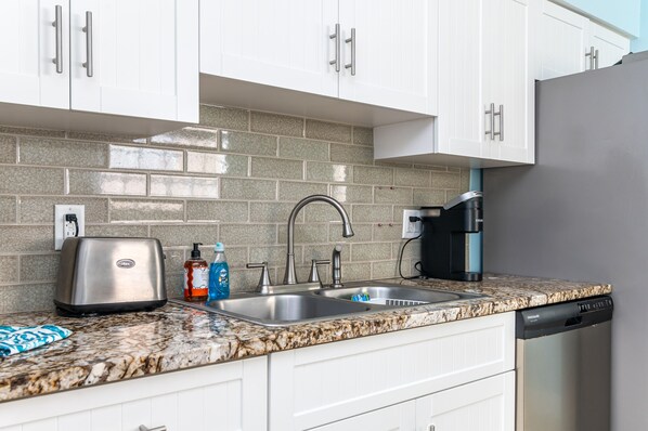 A kitchen with white cabinets, a granite countertop, a toaster, a sink, and a dishwasher.