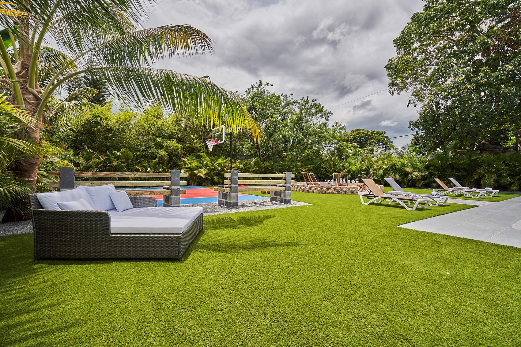 Un espacio exterior bien cuidado con césped artificial, mesa de billar, sillones de descanso y un sofá de mimbre.