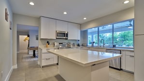 A modern kitchen with a large island, built-in appliances, and a view of the outdoors. - Villa Athena • Basketball Court | Heated Pool (Miami)