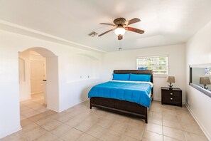 A bedroom with a bed, a ceiling fan, a window, and a nightstand.