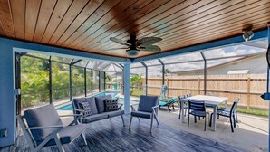 Un patio couvert avec une piscine, un coin salon et une table avec des chaises.