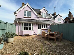 A pink house with a patio, a wooden table, and chairs. - Seagull Cottage (Lyme Regis)