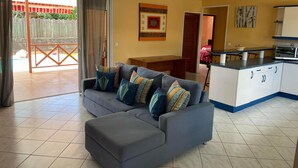 A living room with a grey sofa, a dining table, and a kitchen area with cabinets and a microwave.