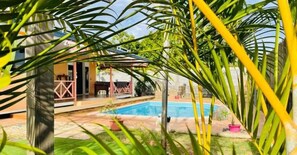 A swimming pool surrounded by lush greenery, a covered patio, and a building with a distinctive pink railing. - TAHITI - Fare Vairai Pool (Faa´a)