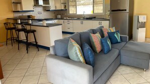 A modern kitchen with a grey sofa, a dining area, and a water dispenser.
