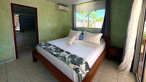 A bedroom with a bed, a window with curtains, a door, and a wall-mounted air conditioner.