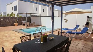 A covered outdoor area with a pool, lounge chairs, and a table set for dining. - Casa La Vista - Relax & Unwind by Villas Now (Playa Blanca)