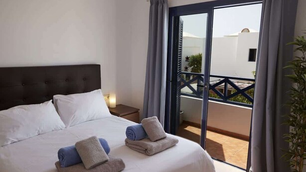 A hotel room with a bed, a nightstand, a balcony with a railing, and a potted plant. - Casa La Vista - Relax & Unwind by Villas Now (Playa Blanca)