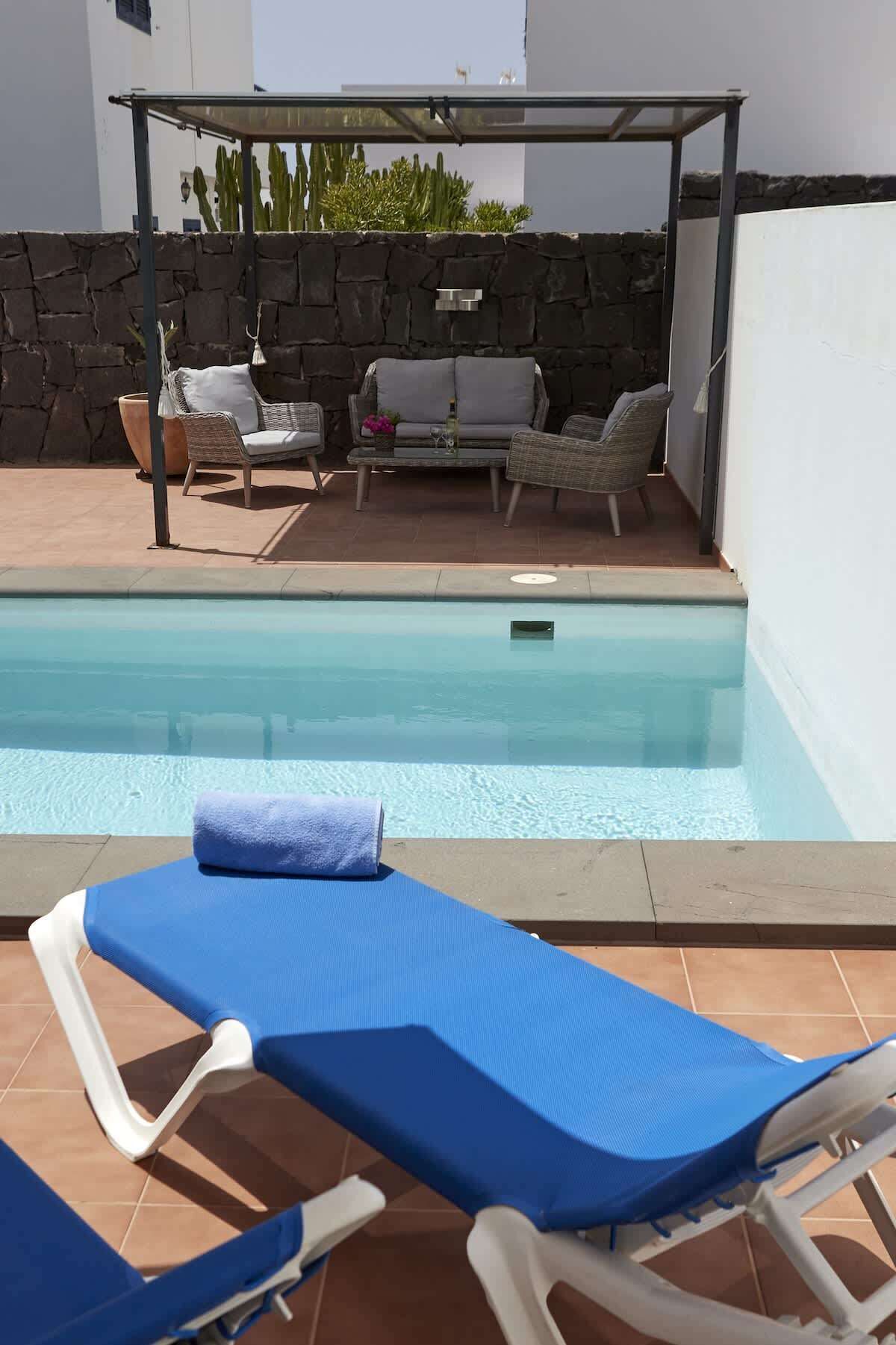 Zona junto a la piscina con sillas de descanso, un espacio de estar techado y un muro de piedra.