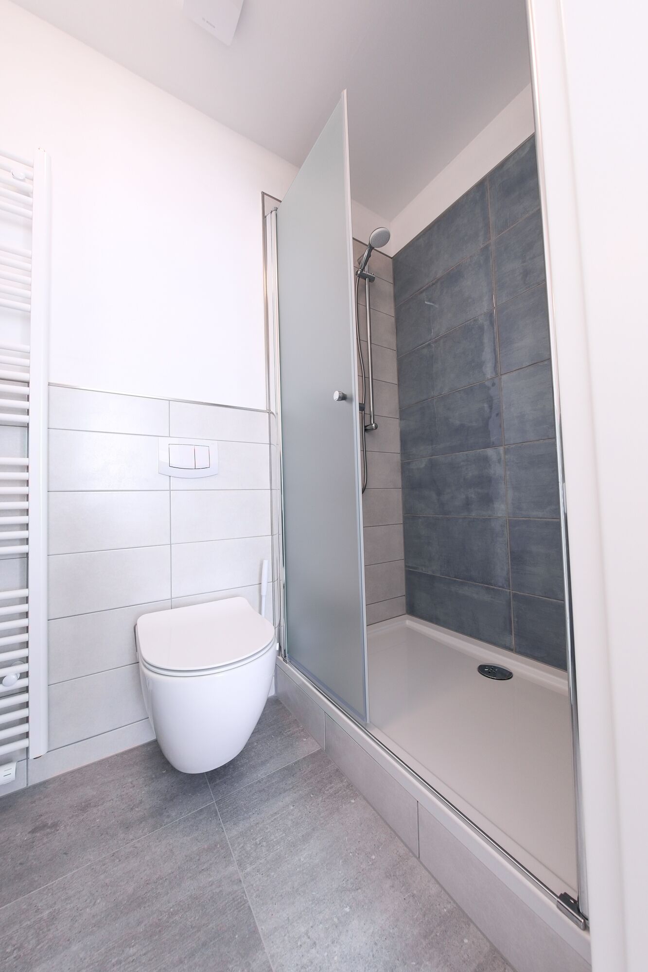 Ein modernes Badezimmer mit Toilette, einer gläsernen Duschkabine und gefliesten Wänden.