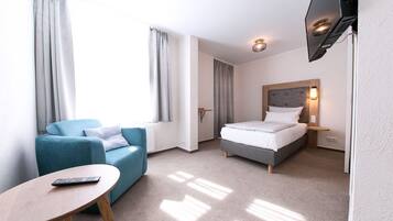Una habitación de hotel con una cama, un sofá azul, una mesita y un televisor.