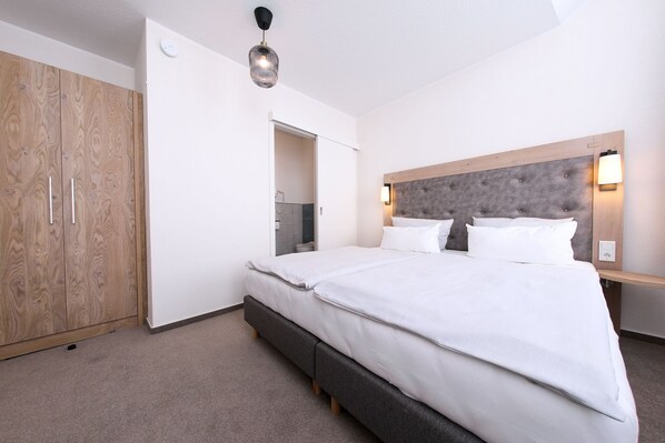 A hotel room with a large bed, a wardrobe, a mirror, and a ceiling light. - 247 selfcheckin Schmiedestrasse (Leer)