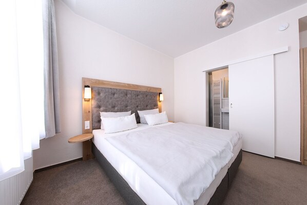 A modern hotel room with a large bed, a wooden headboard, and a walk-in closet. - 247 selfcheckin Schmiedestrasse (Leer)