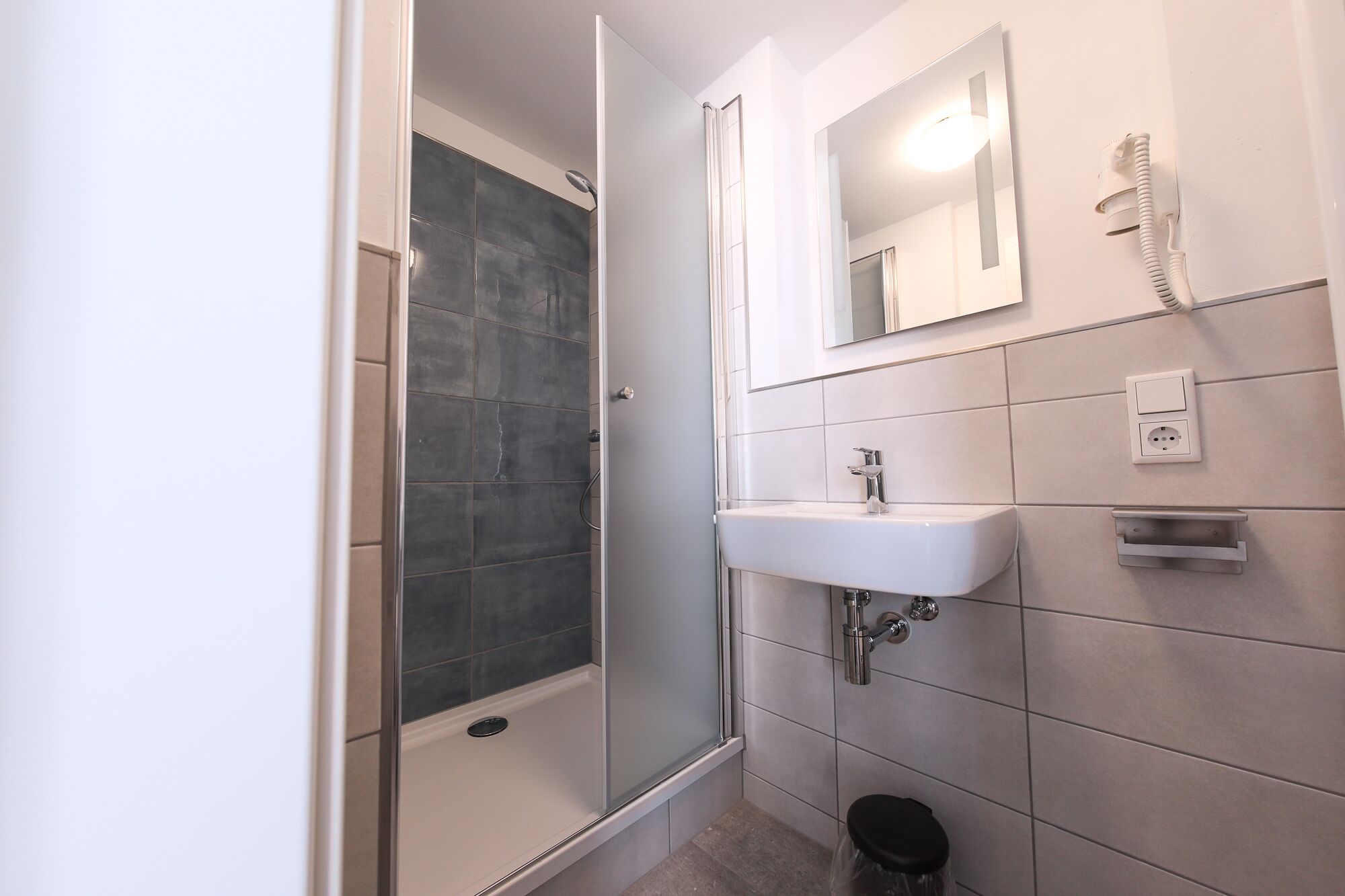 A bathroom with a shower, a sink, a mirror, and a hairdryer.