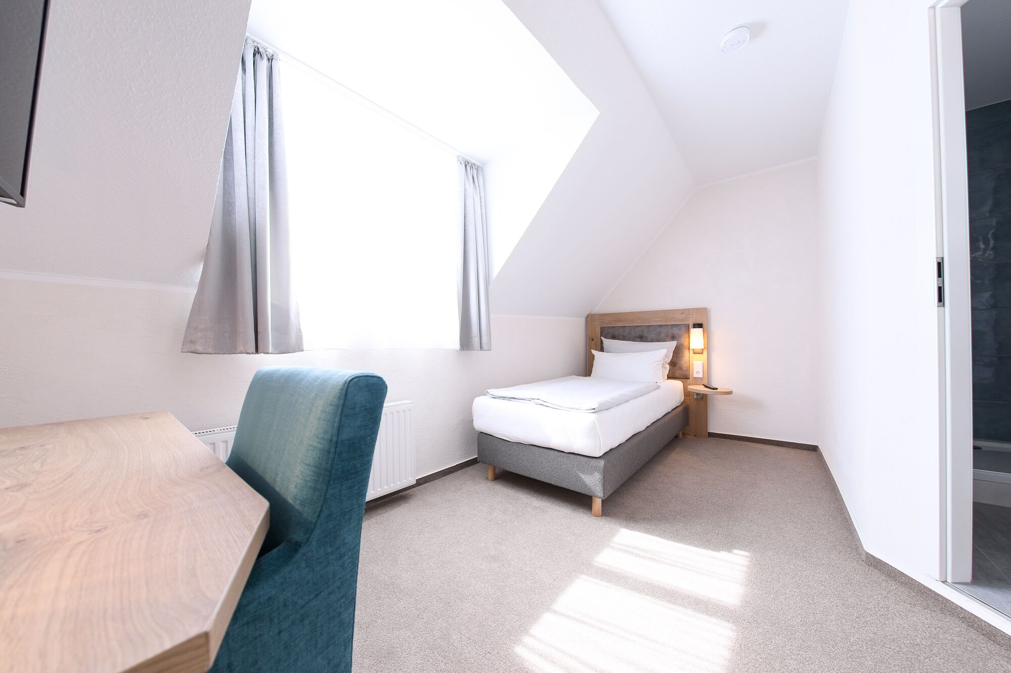 Quarto de hotel com cama, mesa de cabeceira e escrivaninha com cadeira.