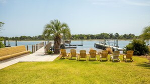 Een terras met stoelen gericht op een waterlichaam, een palmboom en een steiger die in het water uitsteekt.