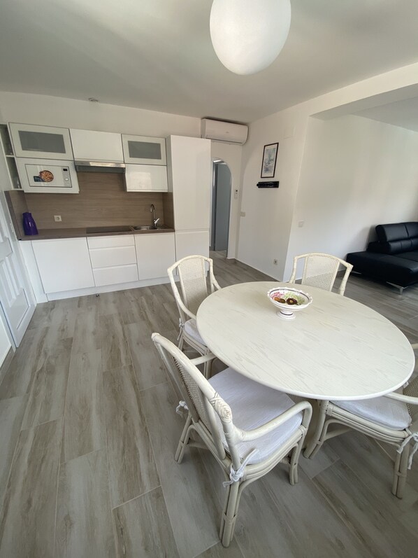 A modern kitchen with white cabinets, a built-in microwave, and a sink. There is a dining area with a round table and four wicker chairs.