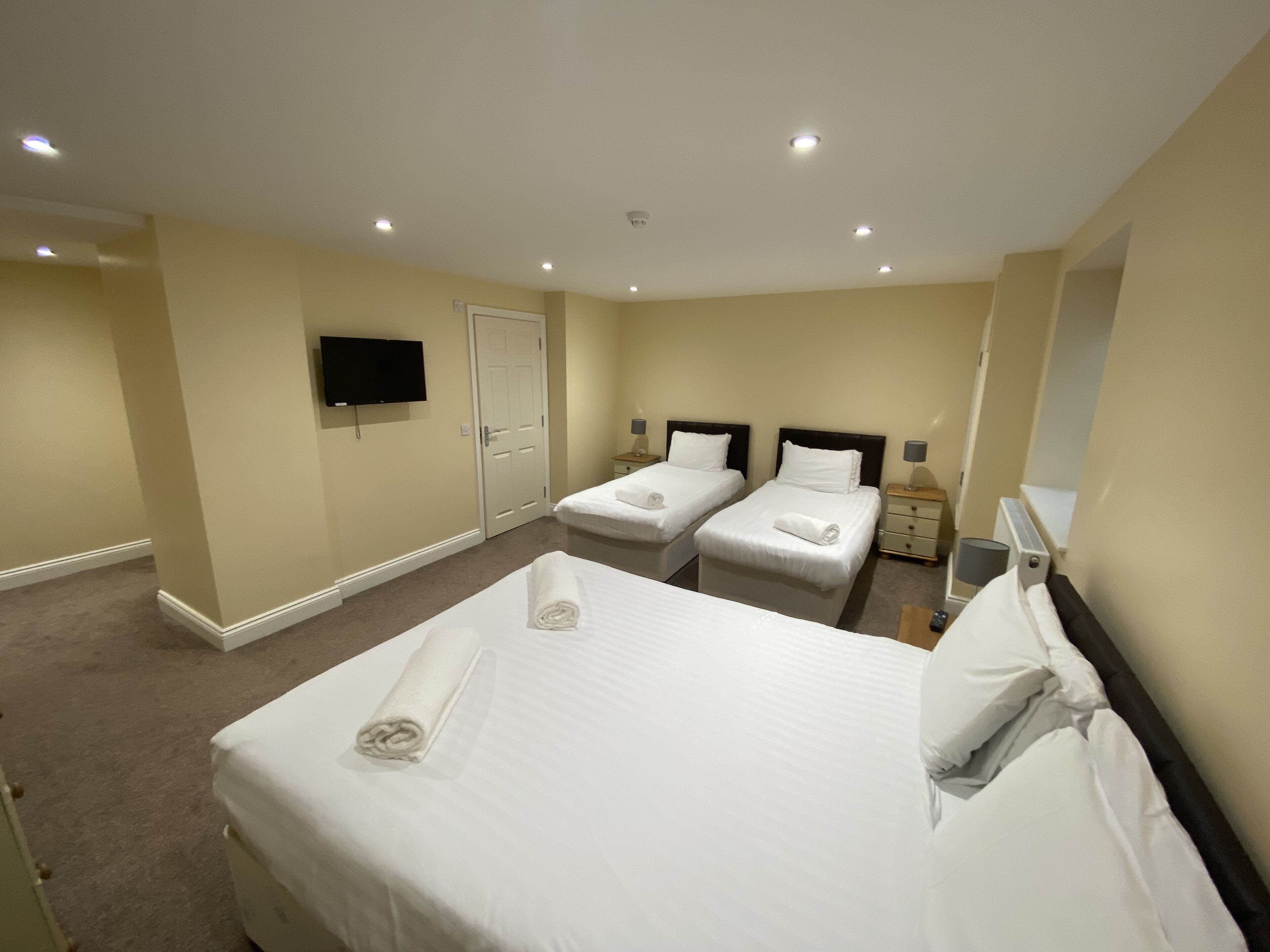 A hotel room with two beds, a television, a door, and a nightstand with a lamp.