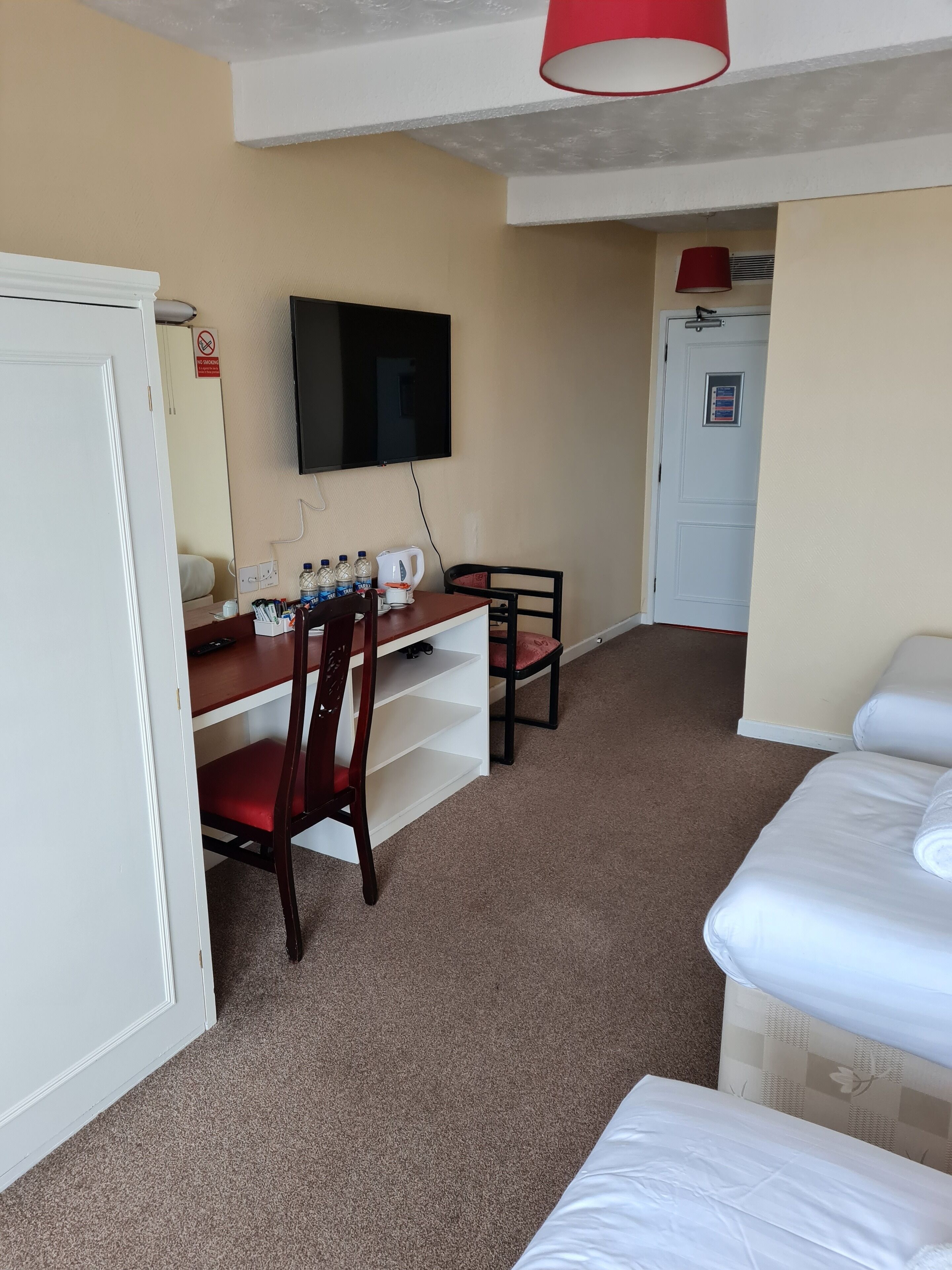 A hotel room with a bed, a desk with chairs, a television, and a door with a sign.