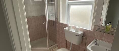 Ein Badezimmer mit Duschkabine, Toilette, Waschbecken und Fenster.