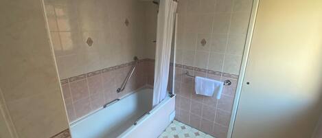 A bathroom with a bathtub, a shower area, and a door.