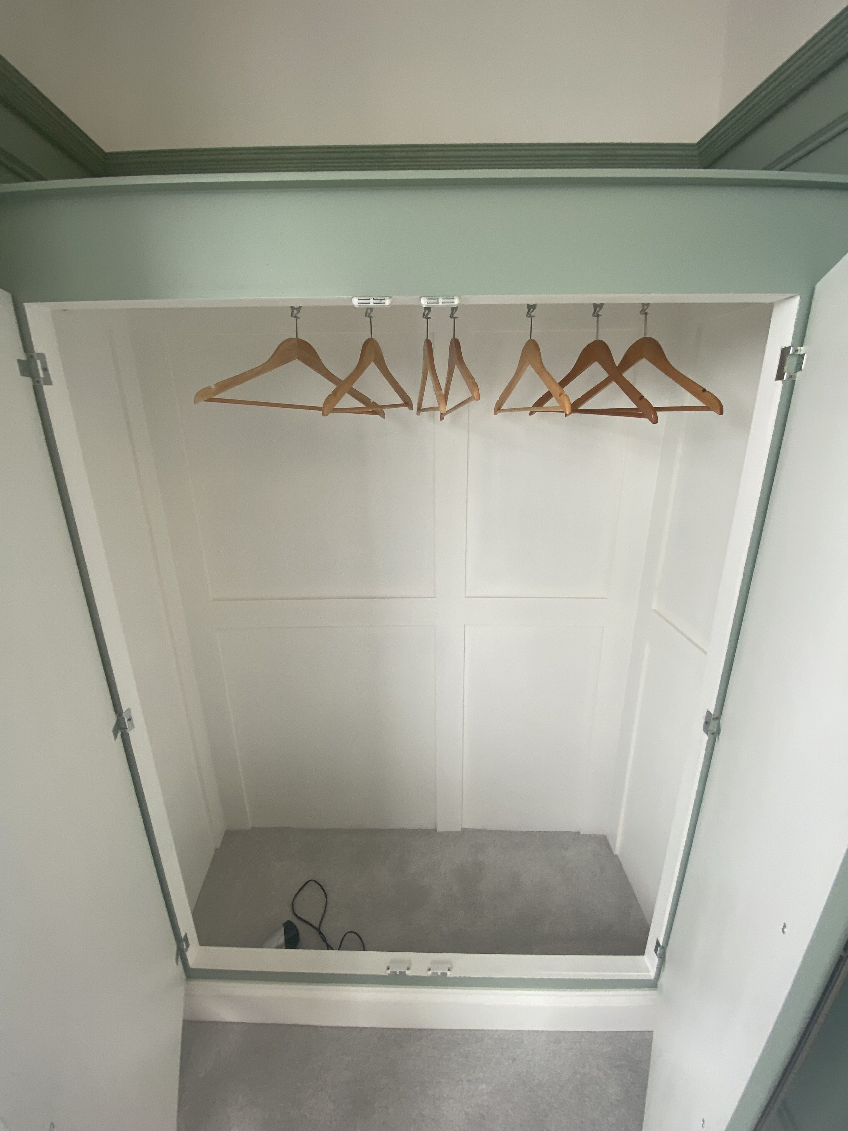 A walk-in closet with wooden hangers on a rod, a grey carpet, and a white door.