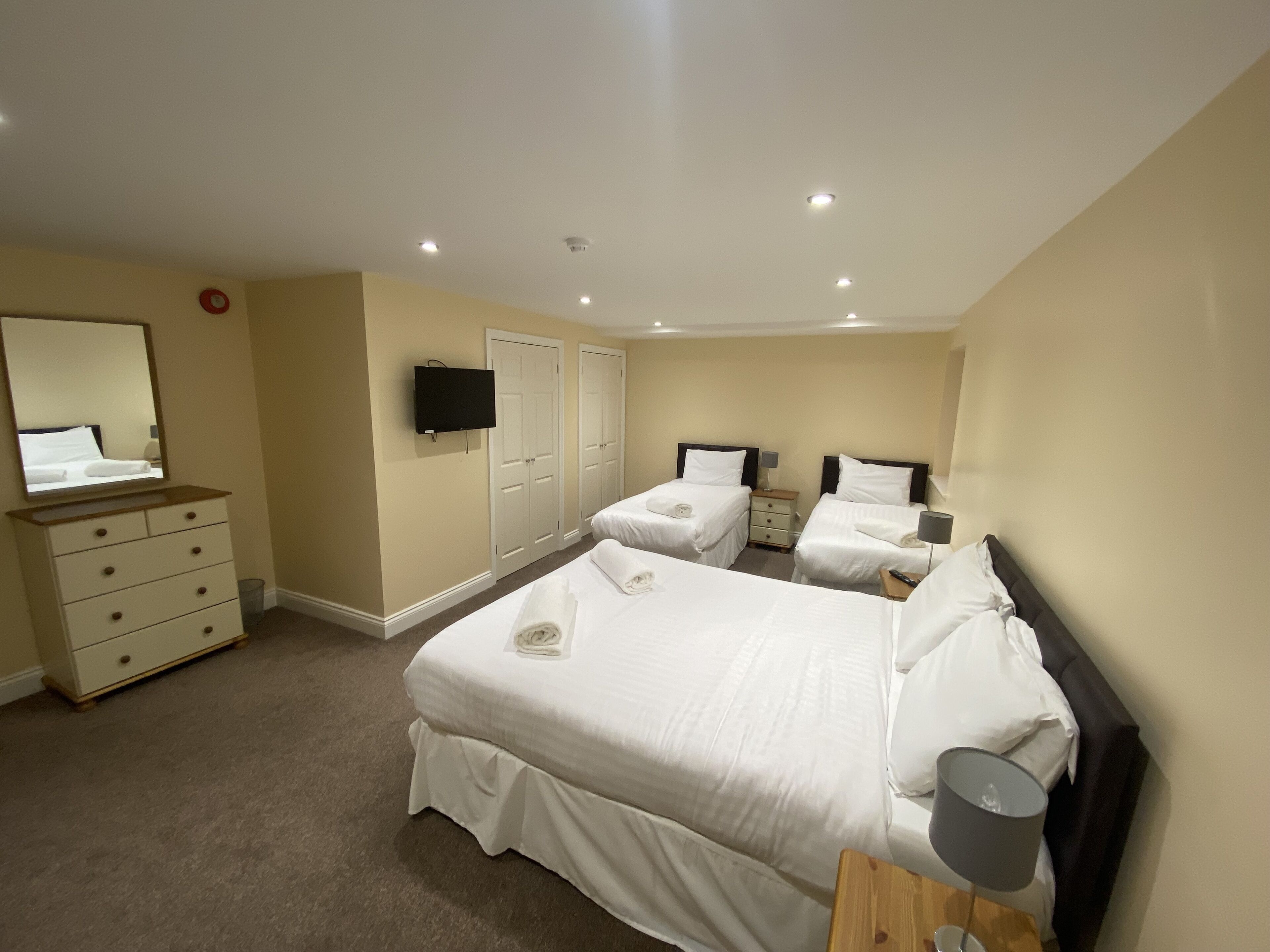 Quarto de hotel com duas camas de solteiro, uma cômoda, televisão presa à parede e um espelho.