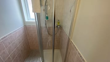 A glass-enclosed shower stall with a handheld showerhead, a handheld soap dispenser, and a glass door.