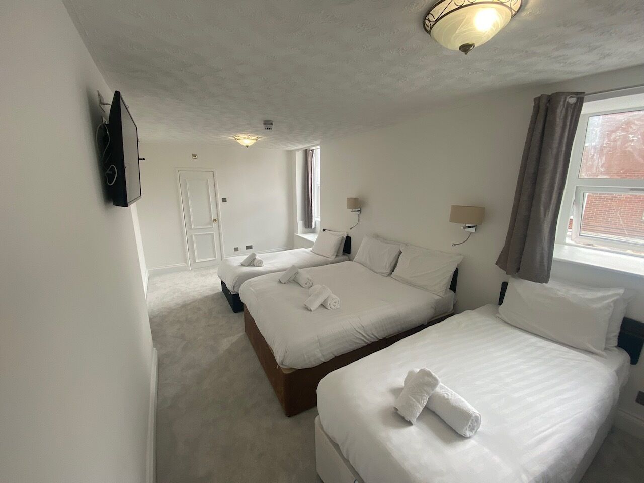 A hotel room with two beds, a television, a window with curtains, and a door.