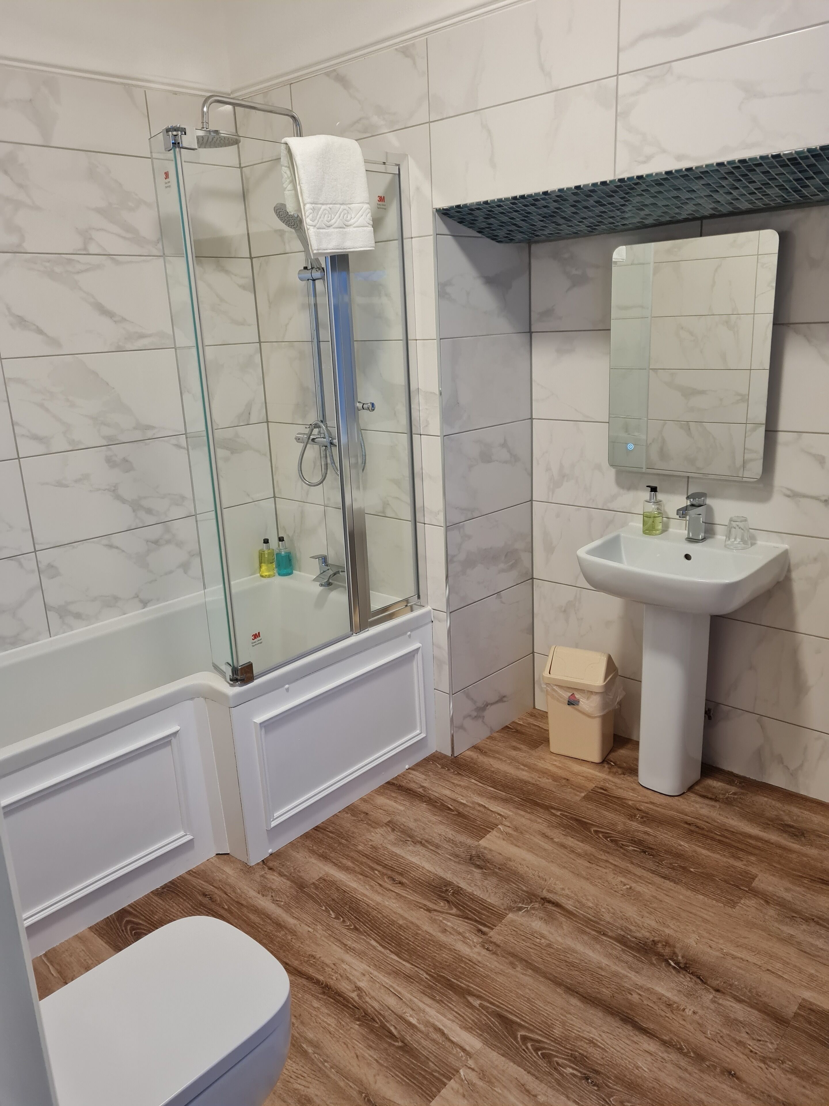 Een badkamer met een douche met glazen wand, een witte wastafel en een toilet.