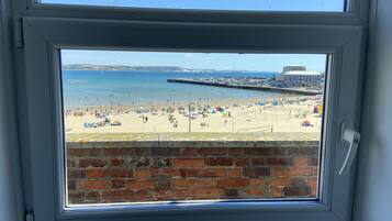 A view through a window of a beach with a brick wall, a pier, and a building in the background.