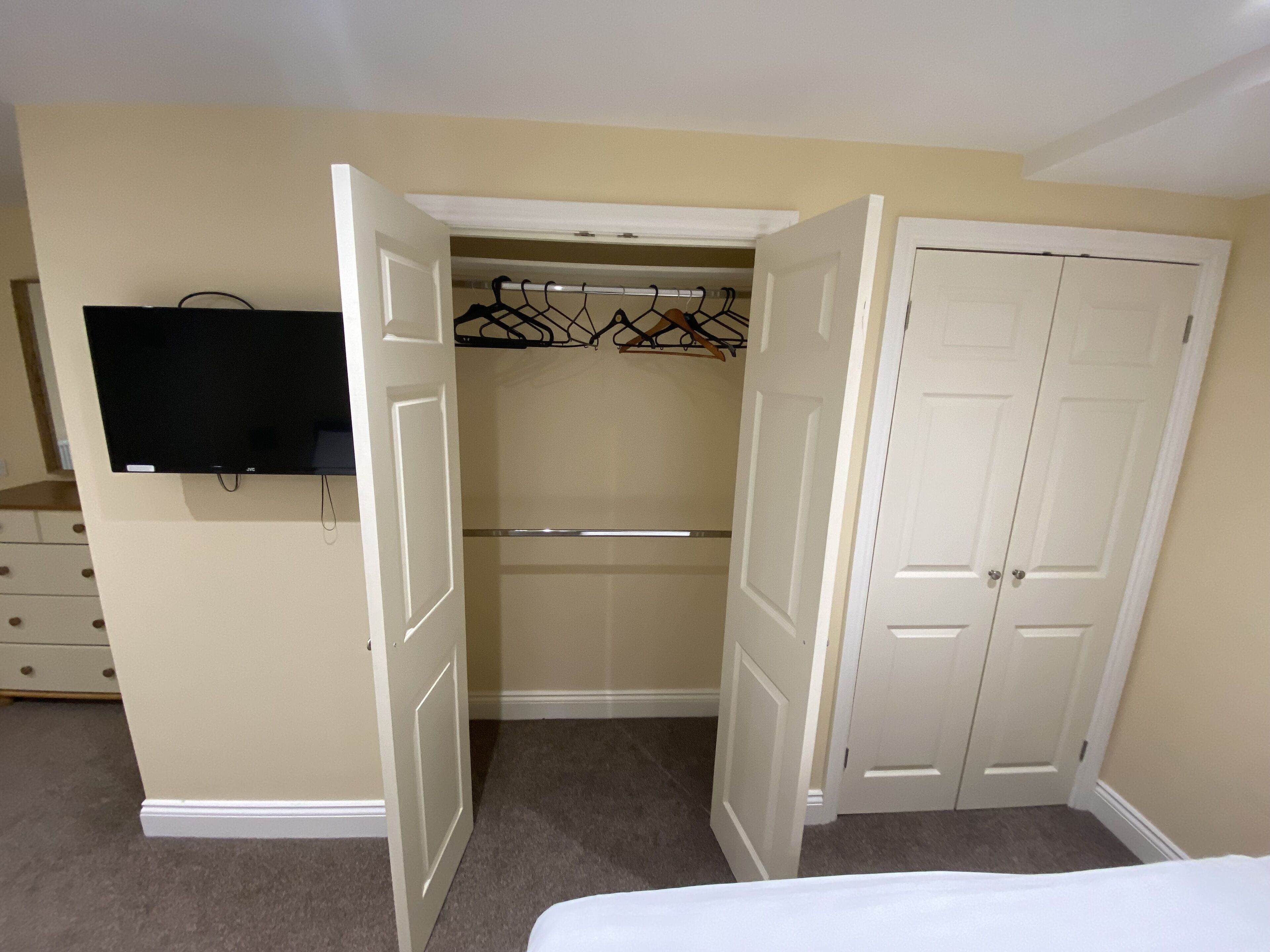 A bedroom with a bed, a TV mounted on the wall, a closet with a hanging rod, and a door.