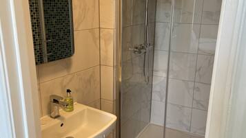 A modern bathroom with a glass-enclosed shower, a pedestal sink, and a tiled floor.