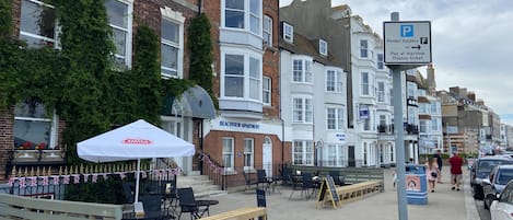 A beachfront apartment building with a terrace, outdoor seating, and a sign indicating parking for permit holders.