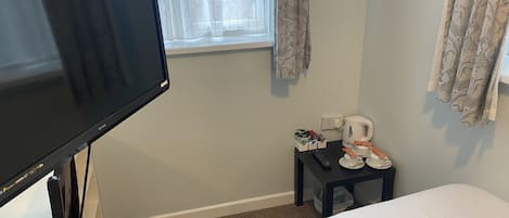 A hotel room with a bed, a TV, a small table with a kettle, cups, and a remote control.