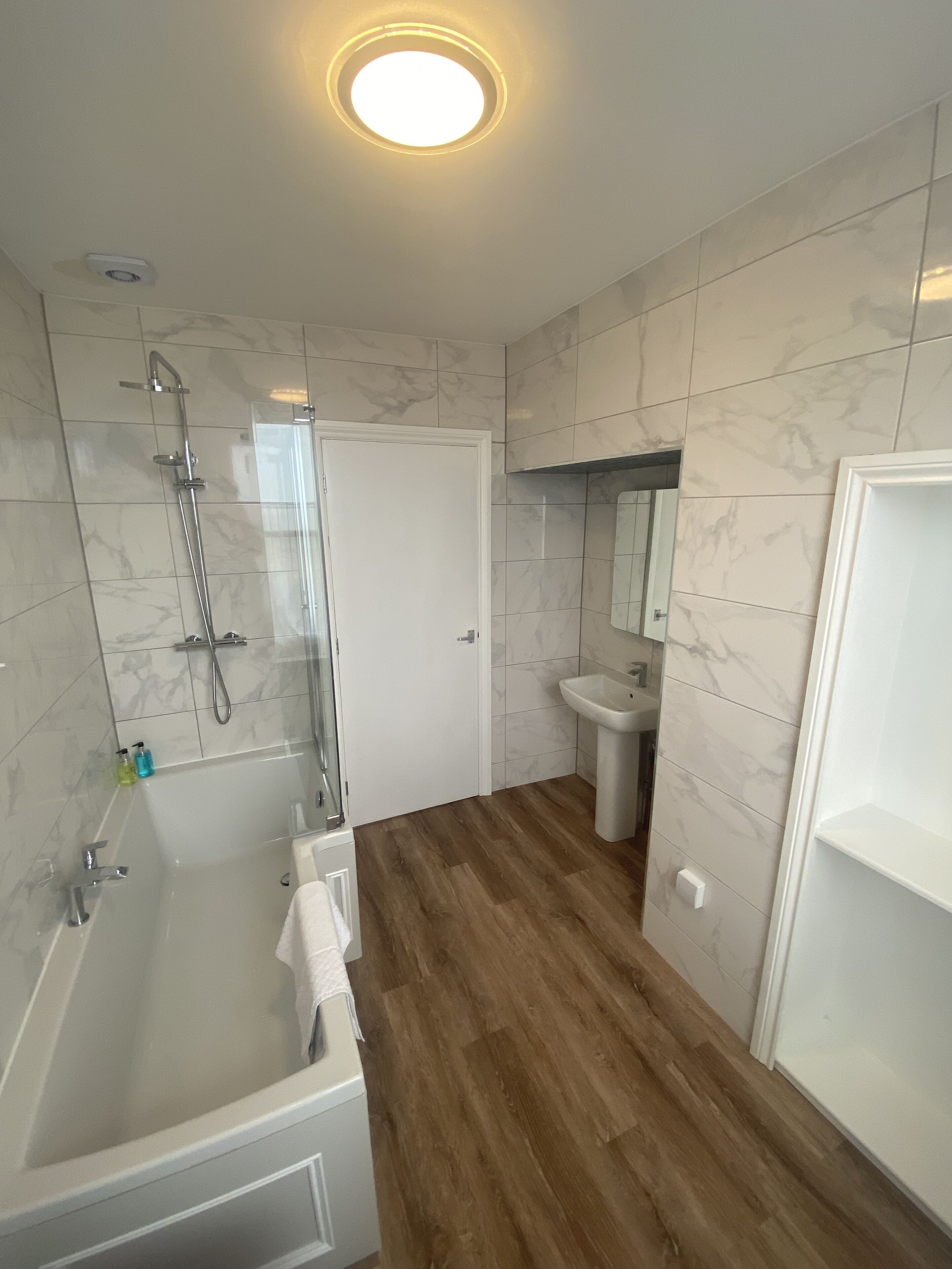 A modern bathroom with a glass-enclosed shower, a white sink, and a wooden floor.